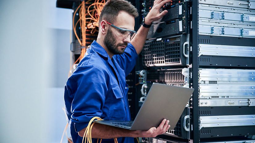 A technician wearing safety goggles works on a TelekomCloud server cabinet.