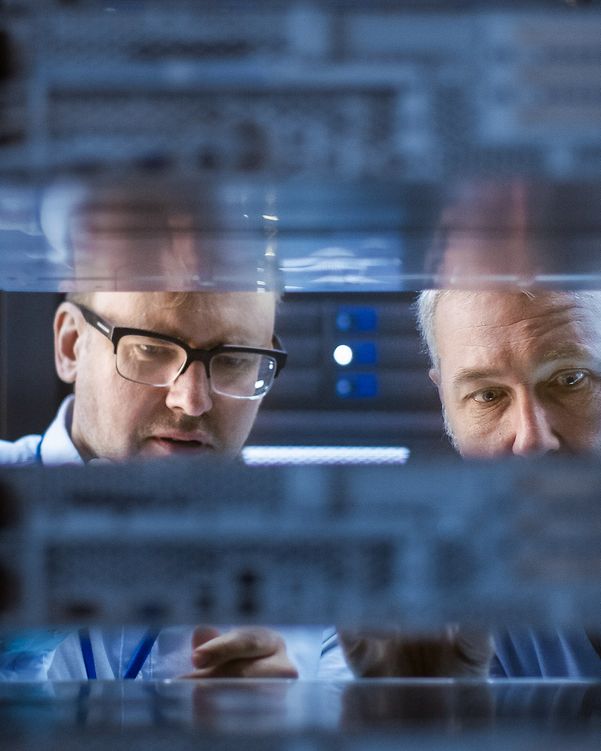 Two men look into a Telekom server cabinet.