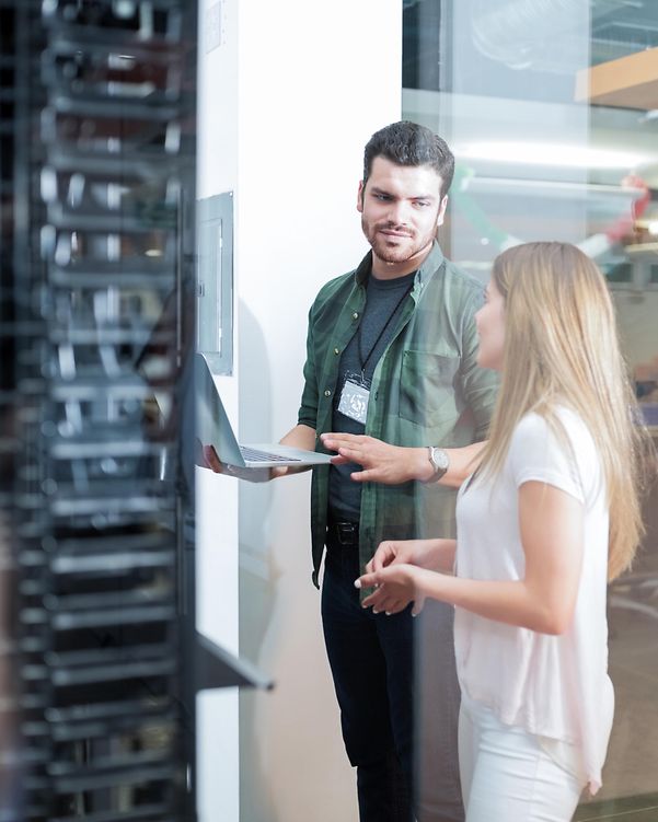 Two people are chatting in front of a large server cabinet about Telekom's managed IT portfolio.