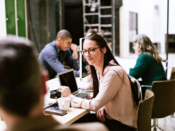 A woman in an open-plan office chats with a colleague about managed IT services.