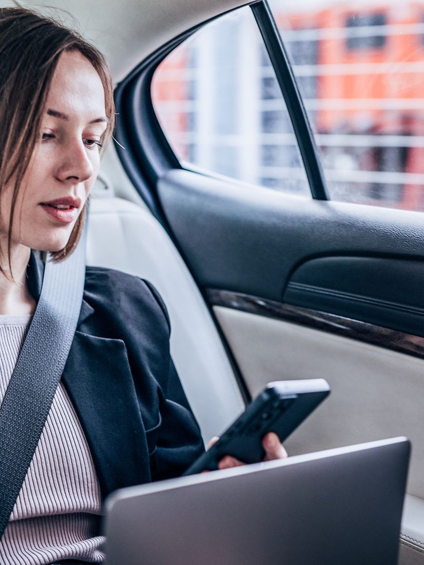 Woman looking at her phone in her car seat with her laptop open
