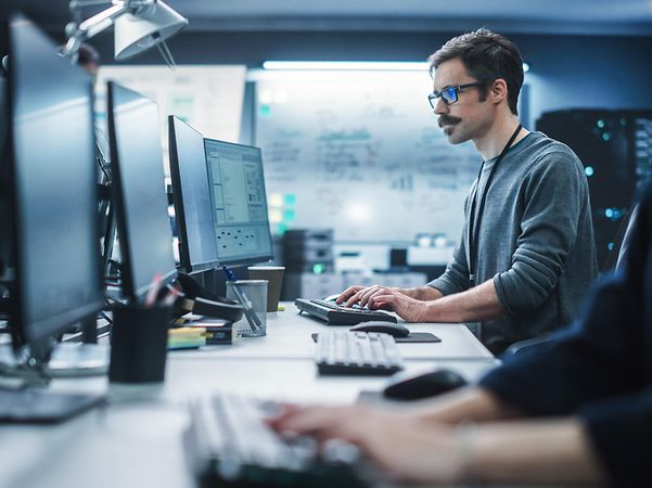 Portrait of a thoughtful engineer working on a desktop computer in a technological office environment.