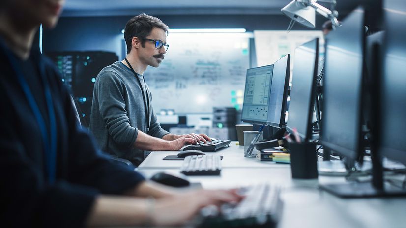 A security specialist works on a desktop computer and monitors IT systems using cyber defence solutions.