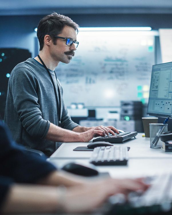 A security specialist works on a desktop computer and monitors IT systems using cyber defence solutions.