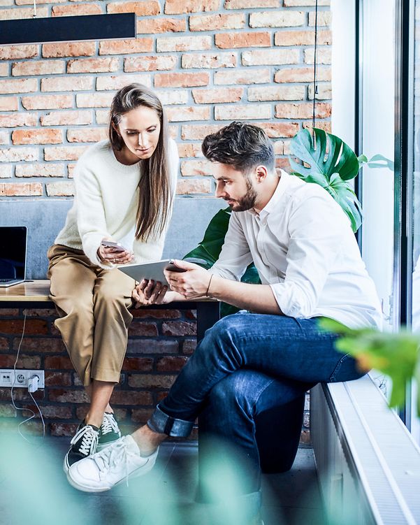 Businessman and businesswoman comparing ideas on a phone and tablet during a meeting in an office