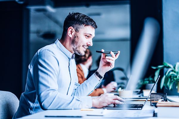 Man in office making phone call, Telekom MDM device registration running on laptop.