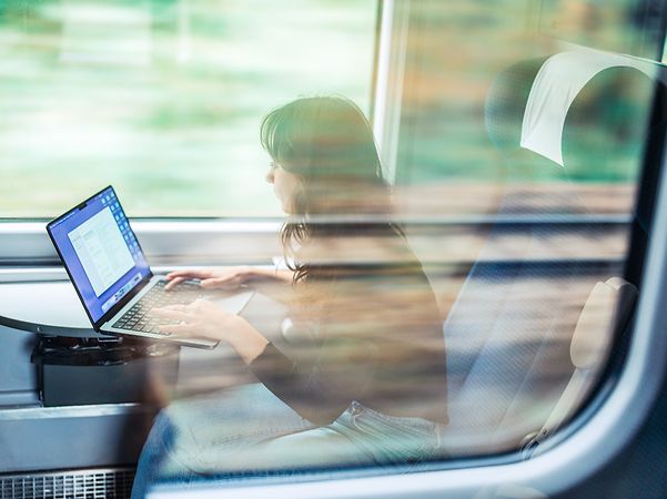 On the train, a woman works intently on her laptop – despite fluctuating network connectivity, everything remains stable.