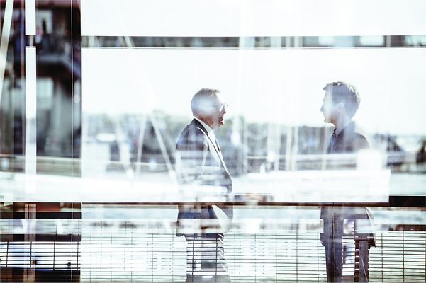 Two men in suits are chatting at the airport about the FreeMove Alliance.
