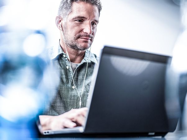 Man with wired headphones working on a laptop with BusinessMail X.400.