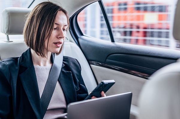 A woman is sitting in her car looking at her mobile phone.
