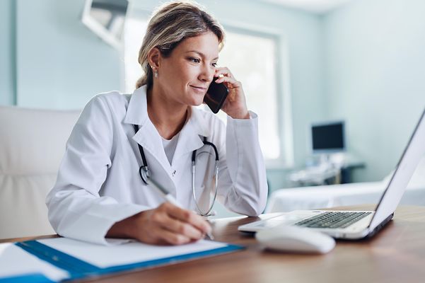 Praxis und Heilberufsausweis Ärztin sitzt in Ihrer Praxis vor einem Laptop