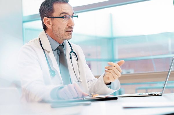 Arzt der in seiner Praxis vor einem Laptop sitzt und die Telematik Lösung der Telekom nutzt