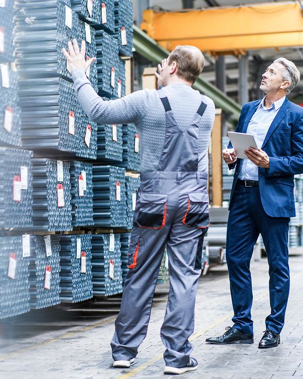Business Analytics Two men are standing in a warehouse in front of several pallets of pipes.