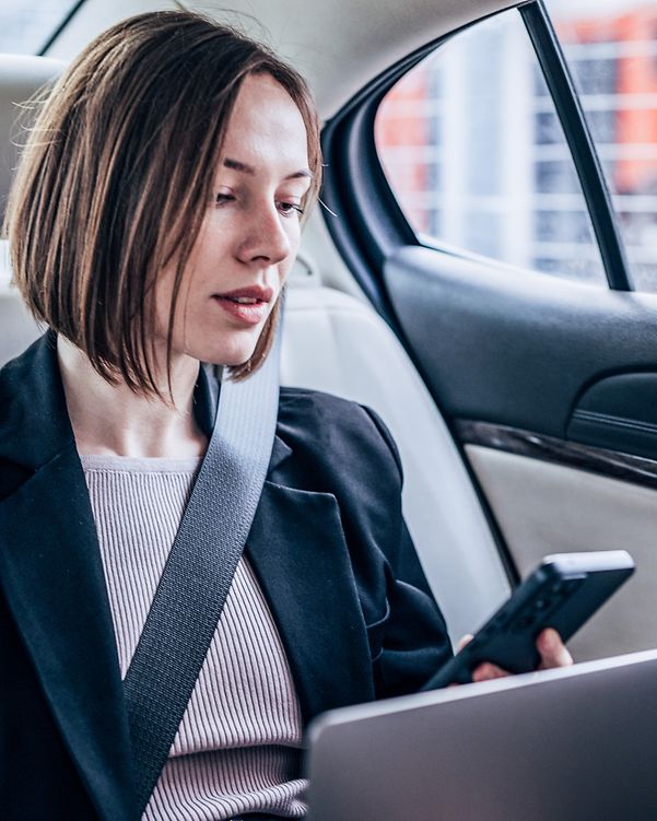Business analytics woman sitting in the back of your car, working on your laptop and looking at your smartphone