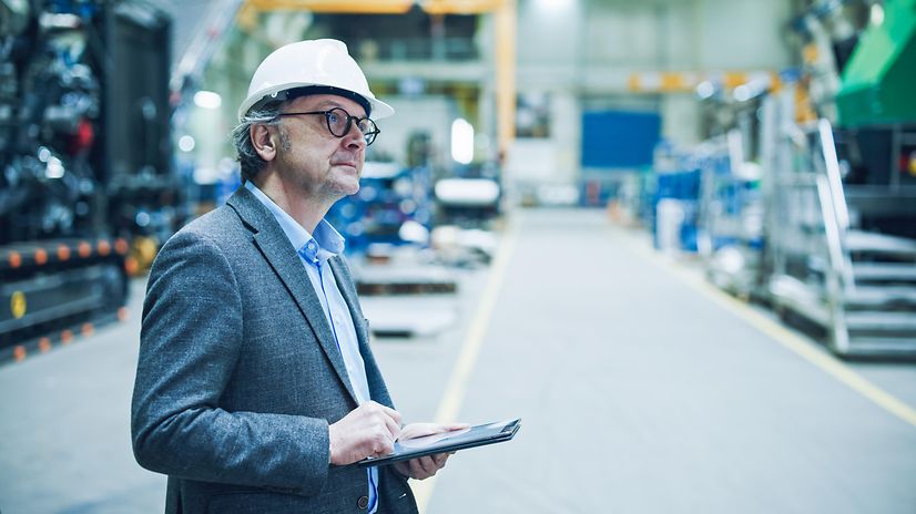 Man wearing a safety helmet stands in a warehouse and monitors the production process.