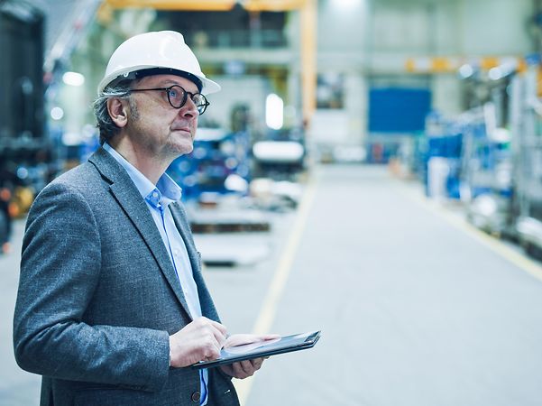 Man wearing a safety helmet stands in a warehouse and monitors the production process.