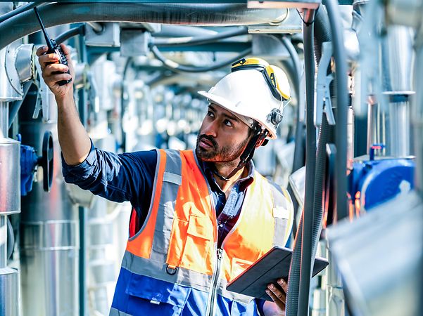 A worker stands in a production facility wearing a helmet on his head.