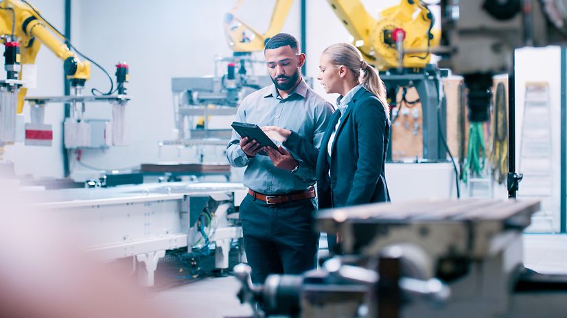 Zwei Ingenieure stehen in einer modernen Fertigungsanlage bei einer Besprechung am Tablet
