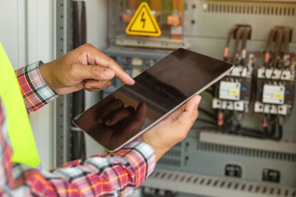 Hands holding a tablet in front of a control cabinet