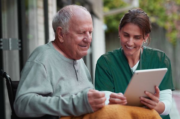 Caregiver and elderly man in wheelchair looking at a tablet together