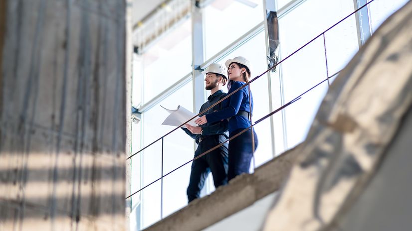 A woman and a man in business attire wearing hard hats are standing in a factory hall.