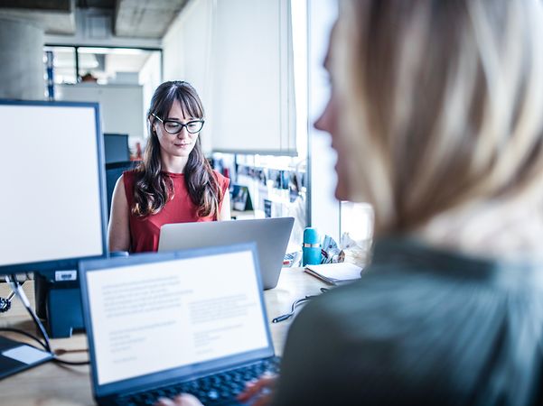 Two women are working together digitally in an office.