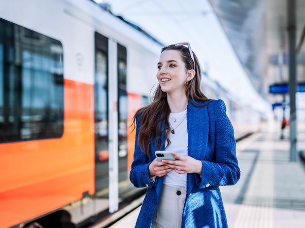 A woman stands in front of a train with her smartphone in her hand.