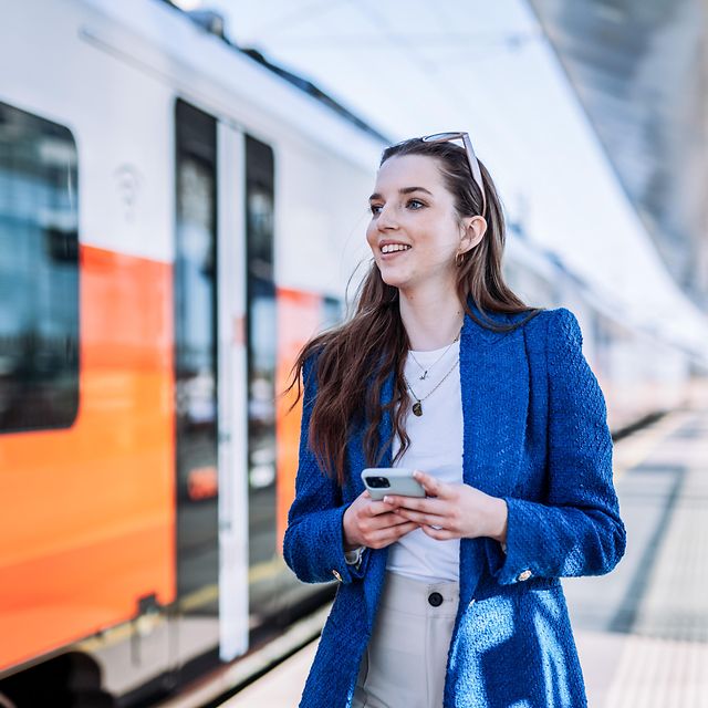 A woman stands in front of a train with her smartphone in her hand.