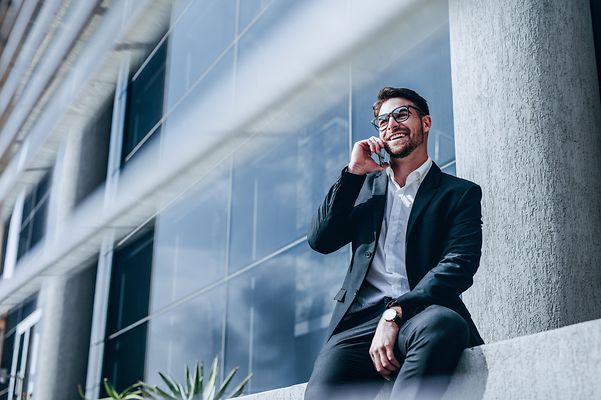 A man is sitting in front of a building and talking on the phone.