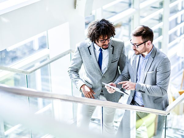 Zwei Menschen unterhalten sich unterwegs aus. Eine Person hat ein Tablet in der Hand.