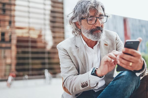 Ein Mann hält ein Smartphone in der Hand und tippt darauf.
