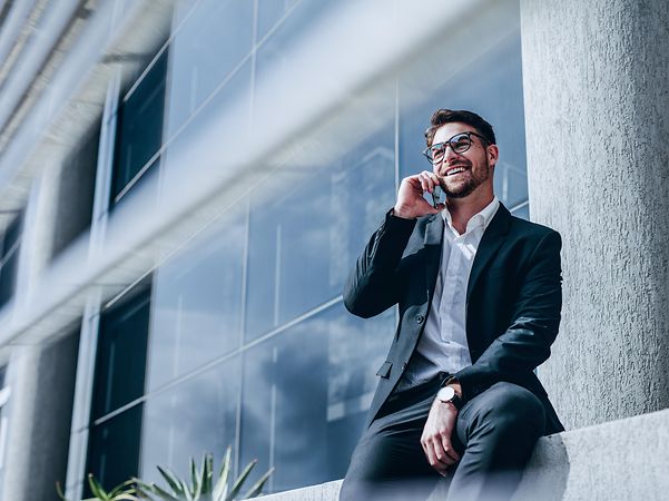 Businessman making a mobile phone call in front of an office building – symbolises mobile availability with a landline number