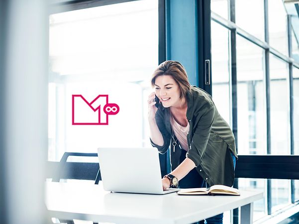 Frau telefoniert und arbeitet am Laptop in modernem Büro, MagentaEINS UNLIMITED Logo im Hintergrund.
