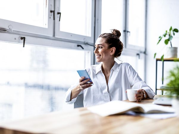 Woman looking out of the window with an iPhone in her hand