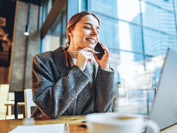 Woman sitting in front of her computer, talking on the phone and surfing the web on Telekom's best 5G network.