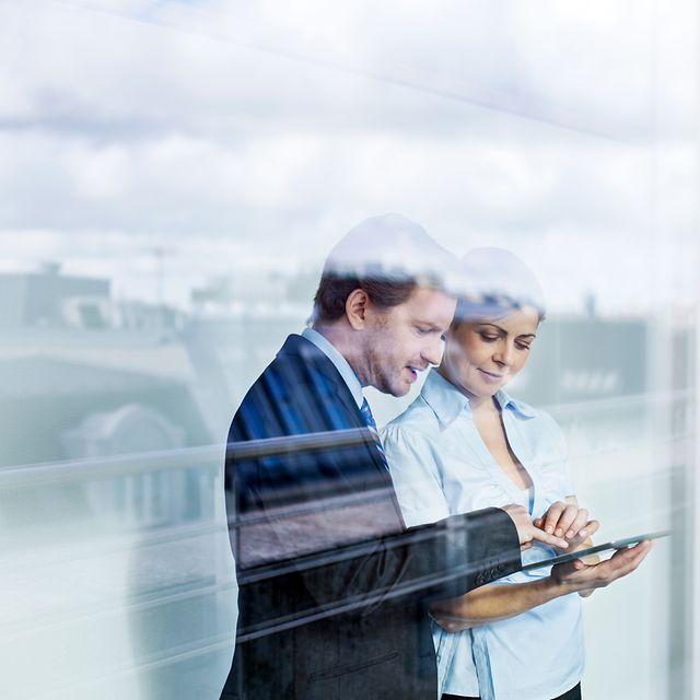 Two adults in business attire look at the Telekom landline tariff advisor and product recommendations on a tablet.