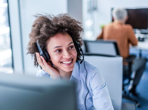 Woman with tousled hair sits smiling with headset in an office