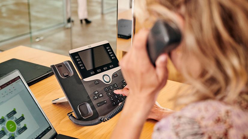 Frau wählt an Festnetztelefon mit Hörer am Ohr