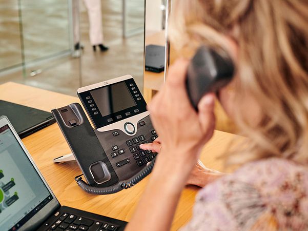 Frau wählt an Festnetztelefon mit Hörer am Ohr