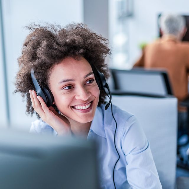 Woman with tousled hair sits smiling with headset in an office