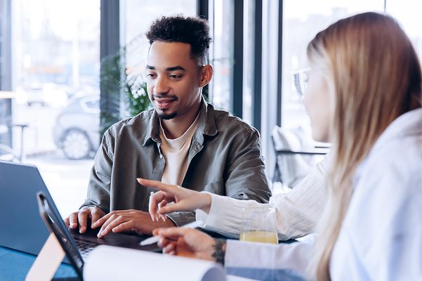 A woman and a man are sitting in front of their laptops and chatting.