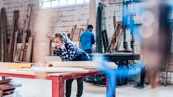 A woman looks at the online orders in her workshop's web shop on her laptop while talking on the phone.