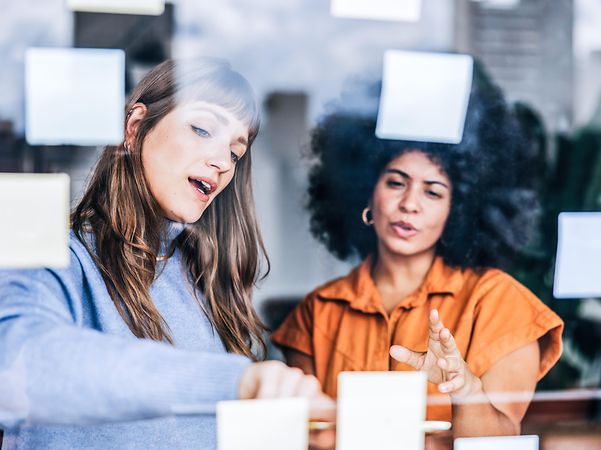 Two women are discussing suitable domain names for their company's website with the help of Post-it notes.