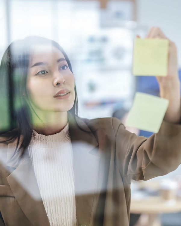 A woman is looking for a suitable domain name for her business and is placing sticky notes on a glass wall for this purpose.