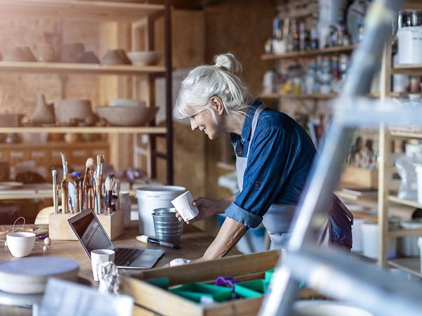 Eine Handwerkerin betrachtet den Webauftritt ihrer Werkstatt auf ihrem Laptop und freut sich über ihre E-Commerce Erfolge.