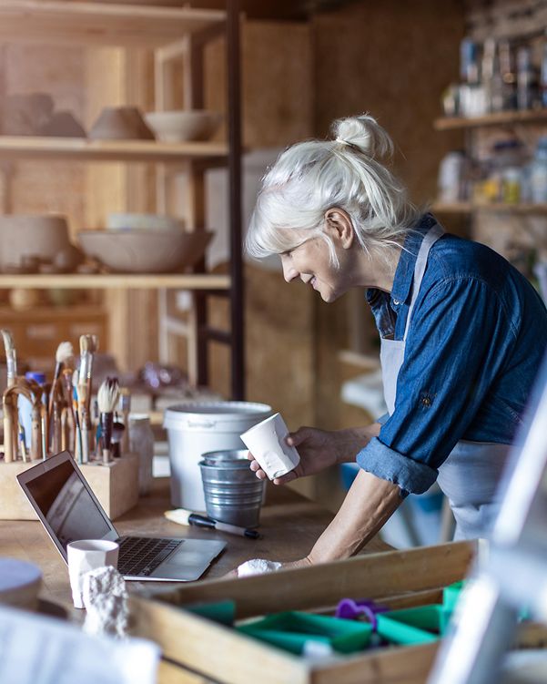 Eine Handwerkerin betrachtet den Webauftritt ihrer Werkstatt auf ihrem Laptop und freut sich über ihre E-Commerce Erfolge.