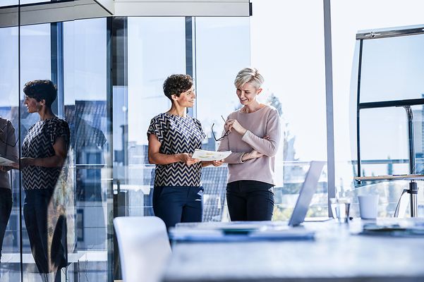 Two smiling businesswomen discussing documents by the window in the office
