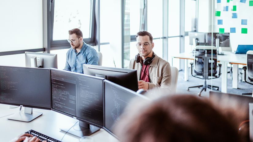 Two men are sitting and looking at their screens.