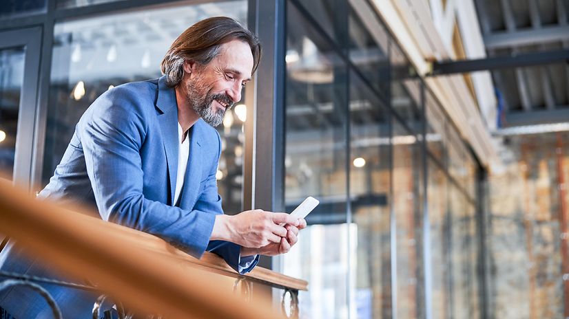 Mann im Businesslook schaut auf sein Smartphone und informiert sich über T Business.