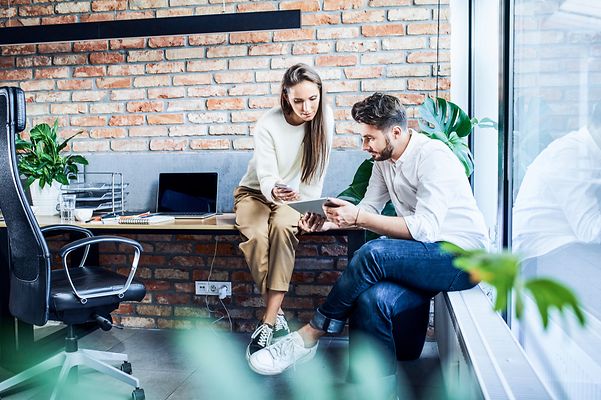 Businessman and businesswoman comparing ideas on a phone and tablet during a meeting in an office